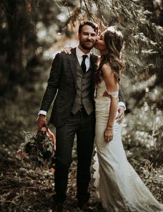 a bride and groom kissing in the woods