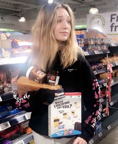 a woman standing in front of a store shelf holding a box of chips and a sandwich