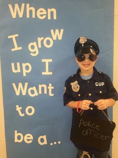 a young boy dressed as a police officer holding a sign that says when i grow up i want to be a cop