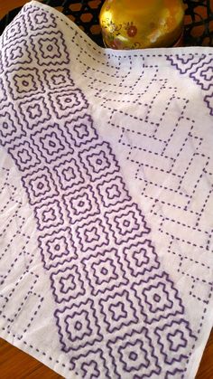 a purple and white table cloth on top of a wooden table next to a vase