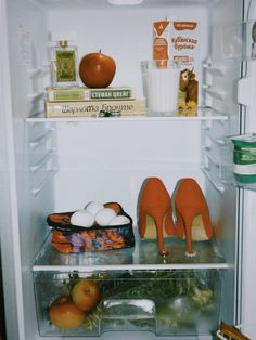 an open refrigerator filled with lots of food and shoes on top of the fridge door