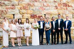 a group of people standing next to each other in front of a stone wall holding bouquets