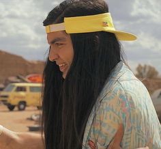 a man with long black hair wearing a yellow visor and holding a cell phone