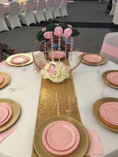 a table set with pink and gold plates, place settings and flowers on the table