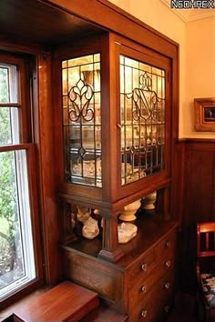 an old fashioned china cabinet with stained glass doors on the top and bottom, in front of a window