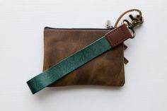 a brown and green leather pouch with a keychain hanging from the front on a white background