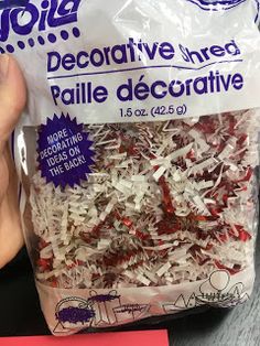 a bag of shredded red and white paper next to a hand holding a pink note