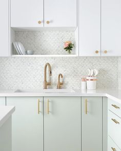 a kitchen with white cabinets and gold handles