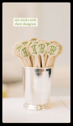 wooden spoons with green letters in a silver cup on a white tablecloth and text that reads, stir sticks with these designs