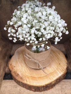 white flowers are in a mason jar on top of a tree stump with burlap