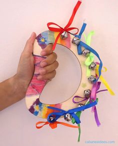 a hand holding a colorful wreath made out of paper with bells attached to the front