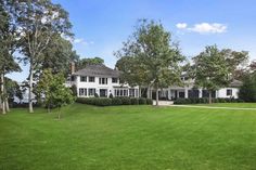 a large white house sitting in the middle of a lush green field next to trees