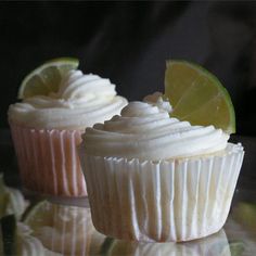 two cupcakes with white frosting and lime slices