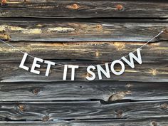 a sign that says let it snow hanging from a clothes line on a wooden wall