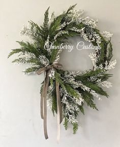 a christmas wreath hanging on the wall with white and green foliage, ribbon and bow