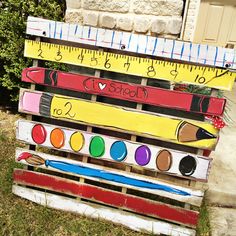 a wooden pallet with rulers and pencils painted on it, sitting in front of a house