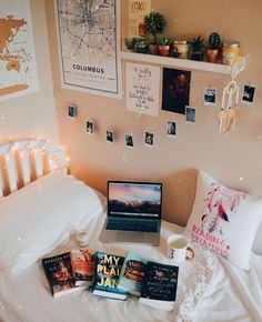 a laptop computer sitting on top of a white bed next to books and pictures hanging on the wall