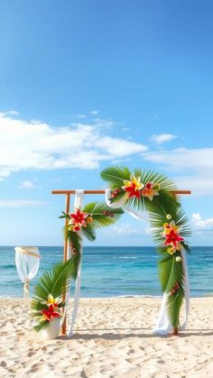 a tropical wedding arch on the beach with red and yellow flowers in front of it