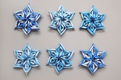 four blue paper snowflakes hanging from strings on a gray wall with white string