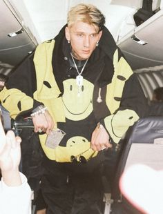 a man in a yellow and black jacket standing on an airplane with his hands out