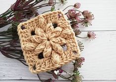 a crocheted square is surrounded by flowers on a white wooden surface with text overlay