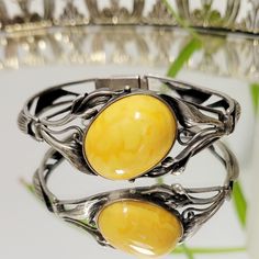 Vintage Art Nouveau 1900s Egg Yolk Amber bracelet! Unmarked intricate lily detailed bracelet that seems to be comprised of sterling silver and Egg yolk amber (possibly Baltic). Absolutely STUNNING rare treasure of a piece in spectacular condition, only minor tarnish on the metal, the face of the amber cabochon has no scratches. .7 oz. Vintage Amber Jewelry With Polished Finish, Vintage Amber Bangle Jewelry, Vintage Baltic Amber Jewelry For Formal Occasions, Vintage Bangle With Polished Finish, Vintage Yellow Cabochon Jewelry, Vintage Yellow Jewelry With Cabochon, Elegant Yellow Bracelet With Intricate Design, Elegant Amber Bracelets For Formal Occasions, Elegant Sterling Silver Cabochon Bracelet