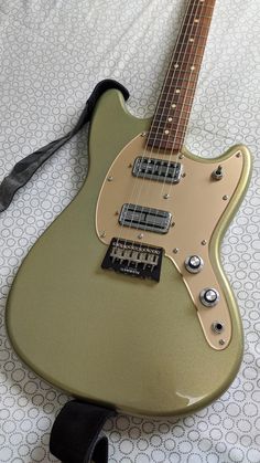 a green electric guitar laying on top of a white bed sheet with a black cord attached to it