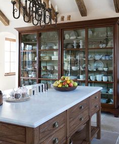 a large kitchen island with a bowl of fruit on it's top and glass front cabinets