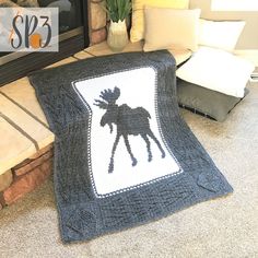 a crocheted moose afghan sits on the floor next to a fireplace with pillows