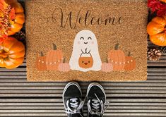 someone is standing in front of a welcome mat with pumpkins and leaves on it