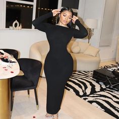 a woman standing in a living room wearing a black dress and heels with her hands on her head