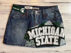 *READY TO SHIP* This ladies size 3 Michigan State University MSU themed denim patch skirt the perfect way to show support to your favorite school! I began with a size 3 gently worn Refuge brand denim skirt and have sewn Michigan State University fabrics on the front & back of the skirt along with a rescued t-shirt piece to create a unique one of a kind design!  The following details & measurements will help you decide if the fit would be right for you!  *Fabric content: 58% cotton/ 40% polyester/ 2% spandex *Waist laying flat: 14" *Around the "outside" of the waistband, through the belt loops: 29" *Hip laying flat: 17.5" *Length (measured from the side): 12" The edges of the fabric pieces will intentionally fray. This gives them the desireable "vintage" fray appearance. The more the skirt Patch Denim Skirt, Senior Painted Jeans, Patch Skirt, Bed Party, Jeans Patch, Central Michigan University, Rush Week, Patch Denim, Painted Jeans