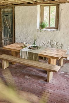 a wooden table and bench in a room with brick flooring, an open door and windows