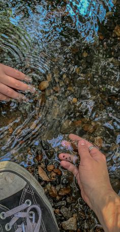 two people are standing in the water with their feet up on some rocks and pebbles