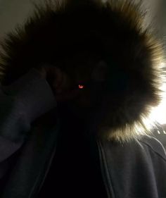 a person wearing a jacket with a fur collar and glowing red eyes in the dark