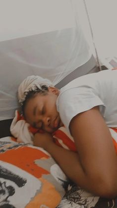 a woman sleeping on top of a bed with an orange and white blanket over her head