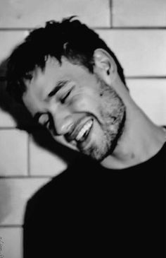 a black and white photo of a man laughing in front of a wall with tiles