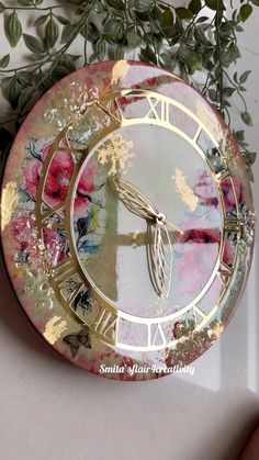 a clock that is on the side of a wall next to some leaves and flowers