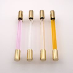 four different colored tubes are lined up on a white surface and one is yellow, the other has pink