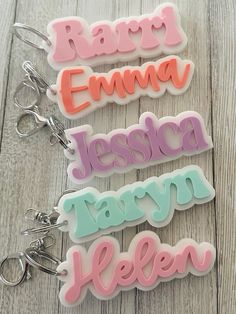 three name keychains with different colors and font on them sitting on a wooden surface