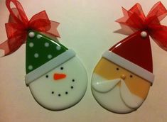 two decorated christmas cookies with red bows on them, one wearing a santa hat and the other as a snowman