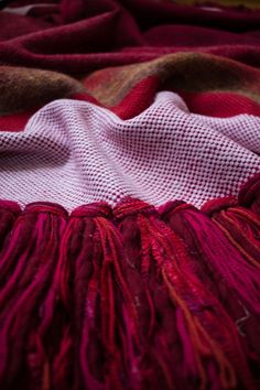 the blanket is laying on top of the bed with red and brown fringes around it