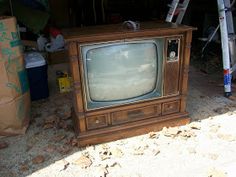 an old tv sitting on top of a wooden stand next to a pile of boxes