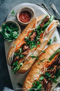 two sub sandwiches with meat, lettuce and carrots on a plate next to dipping sauce