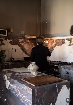 a man standing in a kitchen next to an oven and counter top with a vase on it