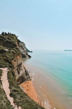 people are walking on the beach next to the water's edge, with cliffs in the background