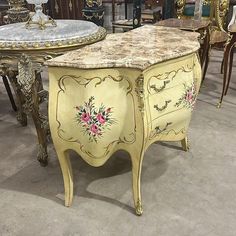 an ornately painted chest of drawers with marble top in a room full of antique chairs and tables