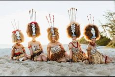 four women in native garb sitting on the beach with their heads made out of feathers