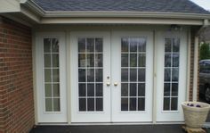 a white double door with two sidelights on the front of a brick building next to a black car