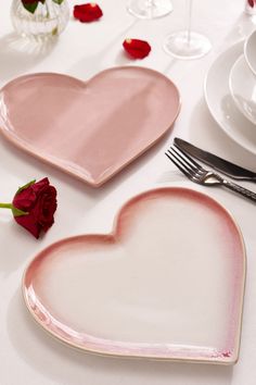 two heart shaped plates on a table with rose petals and wine glasses in the background